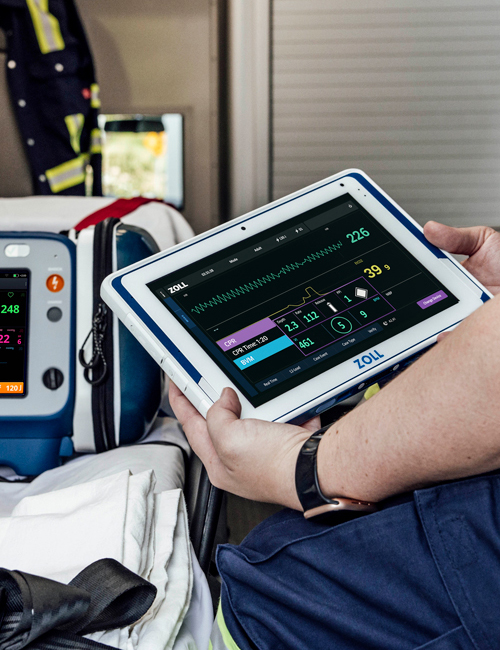 Helsepersonell sitter med et ZOLL Zenix Viewer-nettbrett i hendene ved siden av en Zenix-monitor og defibrillator.